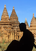 Myanmar, Bagan, Mandalay Division, Silhouette of young woman sitting in front of Buddhist pagodas