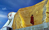 Myanmar, Monyma, Mandalay District, Novice monk praying under giant statue of reclining Buddha in Lay Kyune Sakkyar temple