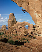 USA, Utah, Arches-Nationalpark, Mann beim Klettern im Sonnenuntergang