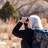 USA, Utah, Escalante, Senior woman uses binoculars while hiking