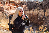 USA, Utah, Escalante, Senior woman uses binoculars while hiking in Grand Staircase-Escalante National Monument