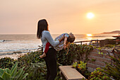 USA, California, Cayucos, Mother holding daughter (4-5) on bluff above beach at sunset