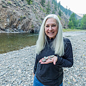 USA, Idaho, Hailey, Porträt einer lächelnden Frau mit herzförmigen Flusssteinen am Big Wood River