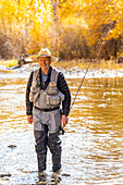 USA, Idaho, Bellevue, Portrait of smiling senior man fly fishing in Big Wood River in Autumn