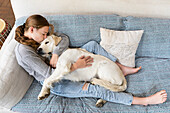 Mädchen (14-15) umarmt English Cream Golden Retriever auf dem Sofa