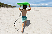 Junge (8-9) mit Surfbrett am Strand