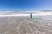 Junge (8-9) mit Surfbrett am Strand