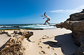 Südafrika, Westkap, Mädchen (16-17) springt von einem Felsen am Strand im Lekkerwater Nature Reserve