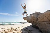 South Africa, Western Cape, Boy (8-9) jumping off rock at beach in Lekkerwater Nature Reserve