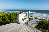 South Africa, Western Cape, Girl (16-17) sitting on boardwalk and putting shoes on in Lekkerwater Nature Reserve