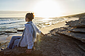 South Africa, Western Cape, Girl (16-17) sitting on beach at sunset in Lekkerwater Nature Reserve