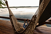 Africa, Zambia, Livingstone, Boy (8-9) relaxing in hammock by Zambezi River