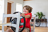 Junge (8-9) spielt mit dem Lenkrad im Wohnzimmer