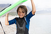 Junge (8-9) trägt Bodyboard am Strand