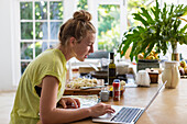 Girl (16-17) using laptop while preparing meal in kitchen