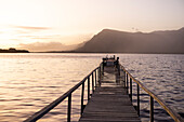 South Africa, Stanford, Boy (10-11) standing on pier at lagoon at sunset