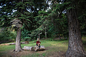 Schweiz, Schweizer Alpen, Appenzell, Mann sitzt auf Baumstamm zwischen Tannenbäumen