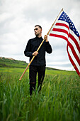 Junger Mann mit amerikanischer Flagge in einem Weizenfeld