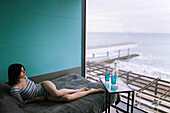 Frau auf dem Bett liegend in einem Hotel mit Blick auf das Meer