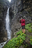 Russland, Karatschai-Tscherkessien, Arkhyz, Kaukasusgebirge, Wanderer fotografiert in der Nähe eines Wasserfalls