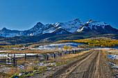 Zaunlinie und unbefestigter Weg Dallas Mountain Straße und San Juan Mountain Range, Colorado, Herbstfarben und Espen leuchtenden Gold.