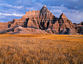 USA, South Dakota, Badlands National Park, North Unit, Gewitterwolken über dem Vampire Peak und herbstlich gefärbte Gräser am frühen Morgen.