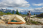 Adult man admiring view from backcountry campsite. Yellow Aster Butte Basin, Mount Baker Wilderness. Mount Shuksan is in the distance. North Cascades, Washington State