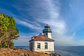 USA, Washington State, San Juan Island, Lime Kiln Point State Park, Lime Kiln Point Lighthouse and rocky shoreline beneath a cirrus filled sky.