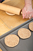 Frau rollt Mehrkornbrotteig zu Kreisen aus, um Hamburgerbrötchen herzustellen (MR)