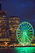 USA, Bundesstaat Washington, Seattle. Die Skyline der Innenstadt in der Abenddämmerung, von der Elliott Bay aus gesehen in Richtung Osten, mit dem Seattle Great Wheel.