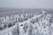 View from above of a car travelling icy road in the middle of the frozen forest covered with snow, Akaslompolo, Kolari, Pallas-Yllastunturi National Park, Lapland region, Finland, Europe