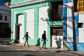 Mann und Frau und ihre Schatten gehen an bunten Gebäuden vorbei, Alt-Havanna, Kuba, Westindien, Karibik, Mittelamerika