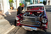 Cuban man inspecting and admiring the open engine of a red classic Chevrolet car, Cienfuegos, Cuba, West Indies, Caribbean, Central America