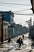 Typical backstreet under panoply of telephone wires, silhouetted family on bike, Trinidad, Cuba, West Indies, Caribbean, Central America