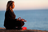 Frau praktiziert Yoga-Meditation am Meer vor Sonnenuntergang als Konzept für Stille und Entspannung, Spanien, Europa