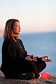 Frau praktiziert Yoga-Meditation am Meer vor Sonnenuntergang als Konzept für Stille, Harmonie und Entspannung, Spanien, Europa