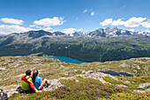 Couple admires lake of Silvaplana and group of Bernina in background, Engadin, Canton of Graubunden, Switzerland