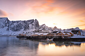 Winterlicher Sonnenuntergang über dem Dorf Sakrisoy mit schneebedecktem Berggipfel, Lofoten, Norwegen, Europa