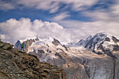 ein Wanderer genießt den ikonischen Gornergrat Gletscher und Monte Rosa während eines bewölkten Sonnenuntergangs, Zermatt, Kanton Wallis, Schweiz, Europa
