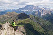 A hiker while photographing at the end fo Via Ferrata delle Trincee, with Civetta Mount on the background, Padon Group, Dolomites, Fassa Valley, Trento Province, Trentino-Alto Adige, Italy.