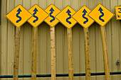 Roadside curve signs leaning on public works building.