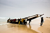 Men unload a fish canoe in the afternoon fish market in Mboro Plage beach when the canoes arrive loaded