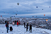 Cappadocia in winter covered with snow, tourists and hot-air balloon taking off near Göreme