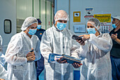 People in PPE looking at packaged products, Fish canning factory (USISA), Isla Cristina, Spain