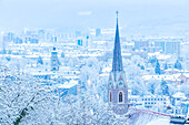 Der Glockenturm von Sankt Nikolaus mit der schneebedeckten Stadt Innsbruck im Hintergrund, Innsbruck, Tirol, Österreich, Europa