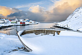 Das Küstendorf Sorvaer ist während des Sonnenaufgangs im kalten arktischen Winter mit Schnee bedeckt (Insel Soroya, Hasvik, Troms og Finnmark, Norwegen)