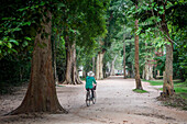 Frau auf dem Fahrrad, Zugang zum Ta Prohm-Tempel, Archäologischer Park Angkor, Siem Reap, Kambodscha
