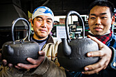 Takahiro Koizumi at left and his assistant Kohei ishimori at right are showing their finish work, iron teapots or tetsubin, nanbu tekki,Workshop of Koizumi family,craftsmen since 1659, Morioka, Iwate Prefecture, Japan