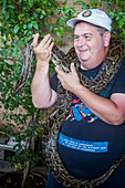 Tourist souvenir photo, Man poses with a Python snake, in Floating Market, Bangkok, Thailand