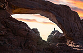 Ein Mann steht in einem natürlichen Arch bei Sonnenuntergang, Arches National Park, Moab, Utah, Nordamerika, USA